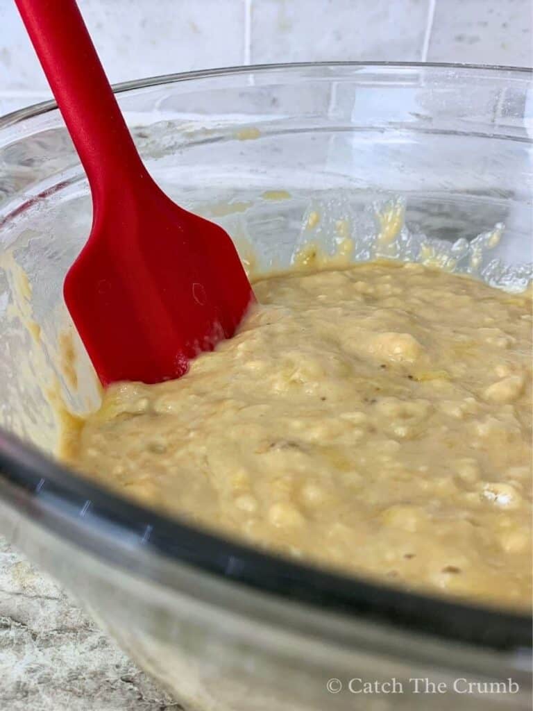 a mixing bowl and spatula with the wet and dry mixtures