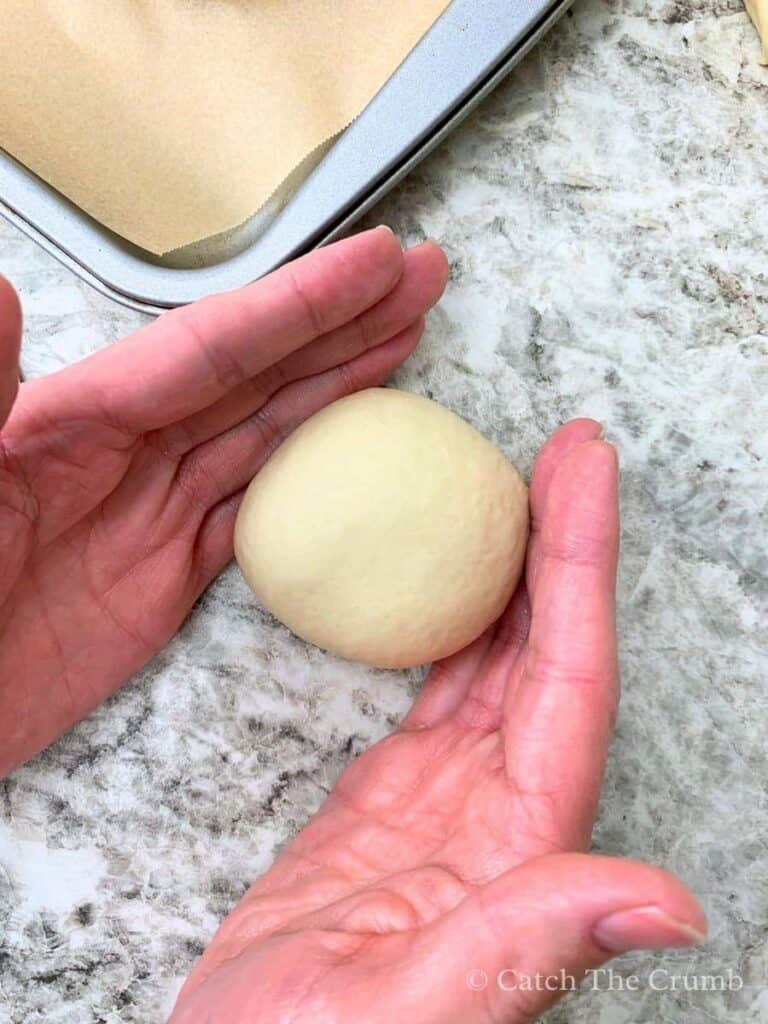 Cupping the dough ball and gently rotating it in small circles on a countertop to create a smooth, round top