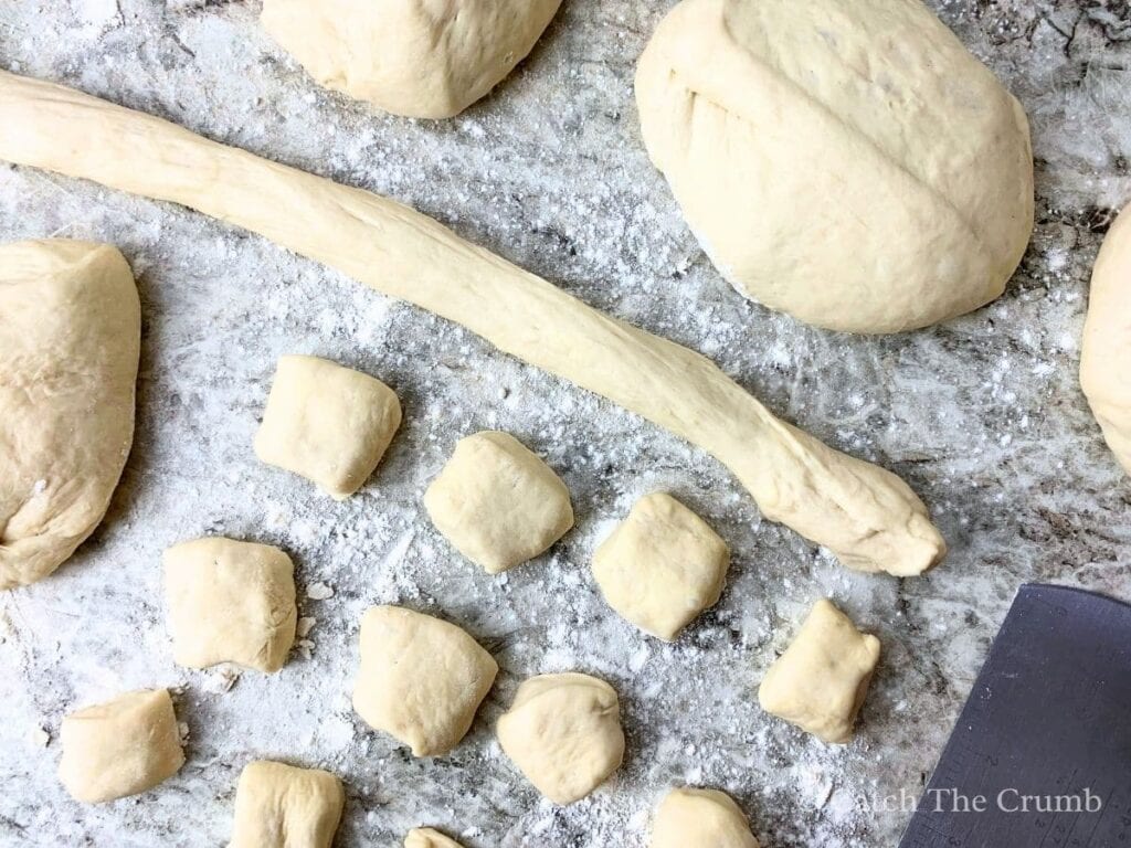 a long rolled up piece of dough, several 1.5 to 2 inch balls and larger dough balls on top of a counter top dusted with flour