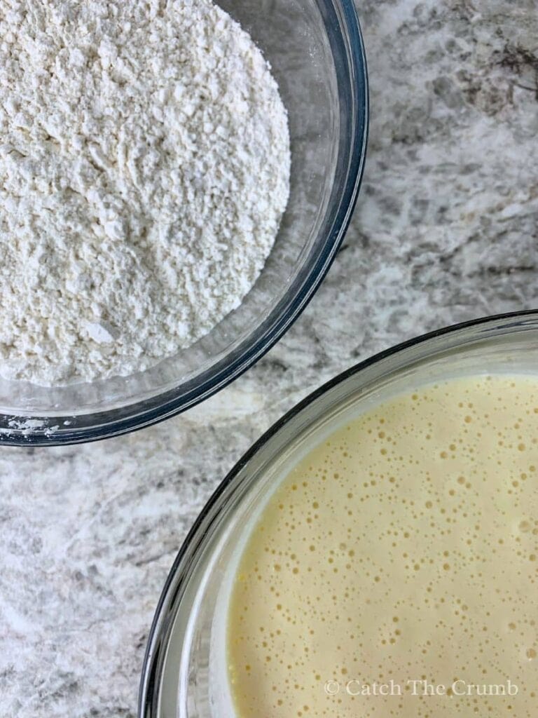 a mixing bowl with flour, baking powder, baking soda, and salt next to a mixing bowl with sugar, eggs, vanilla, and sourdough discard