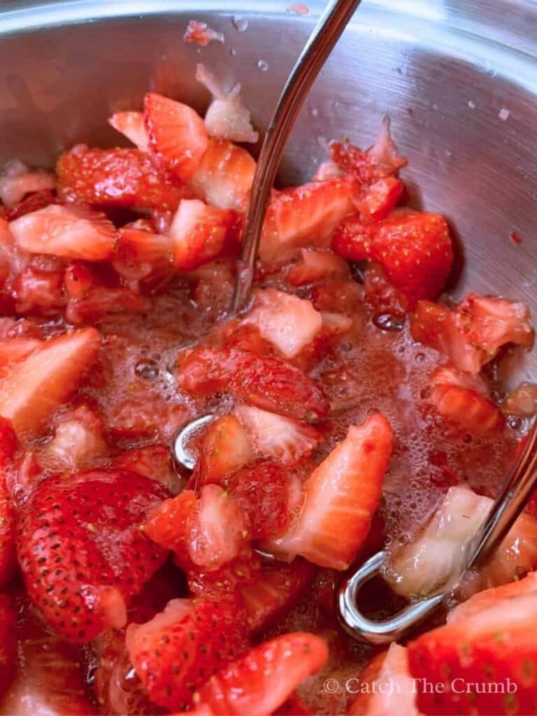 a potato masher mashing strawberries with juices flowing