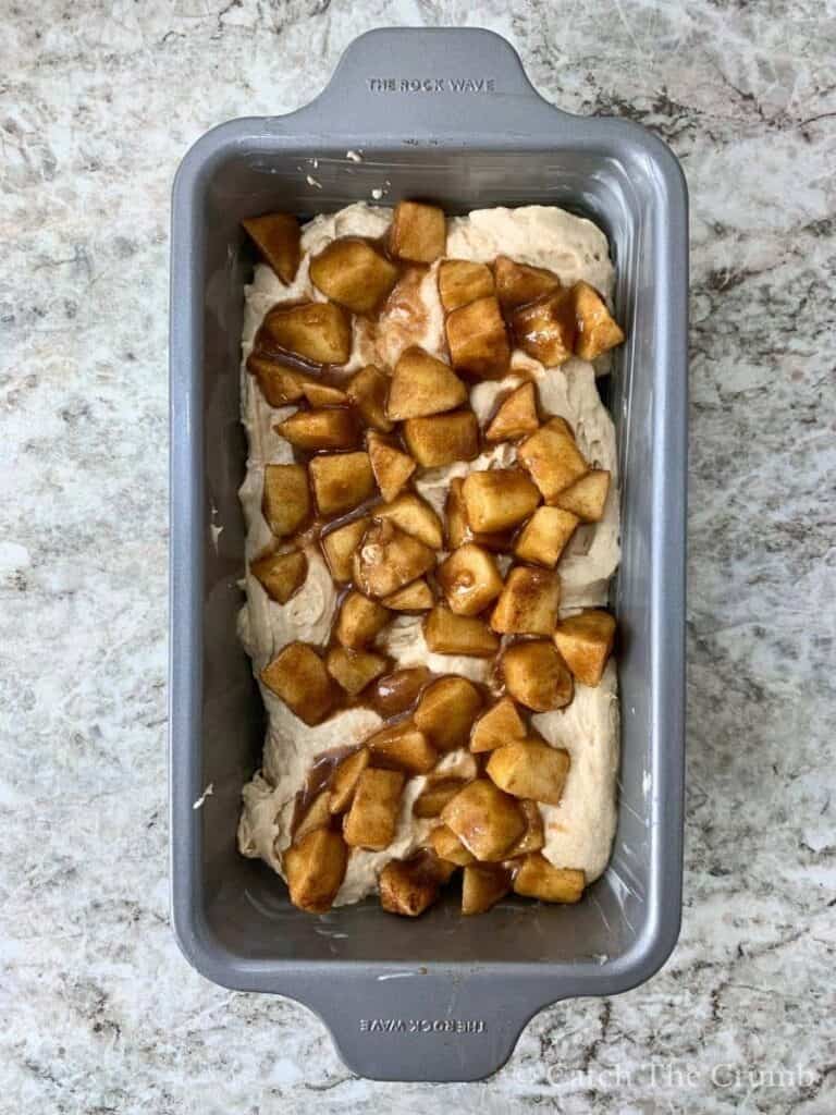 batter spread in a loaf pan with apple mixture spread evenly on top
