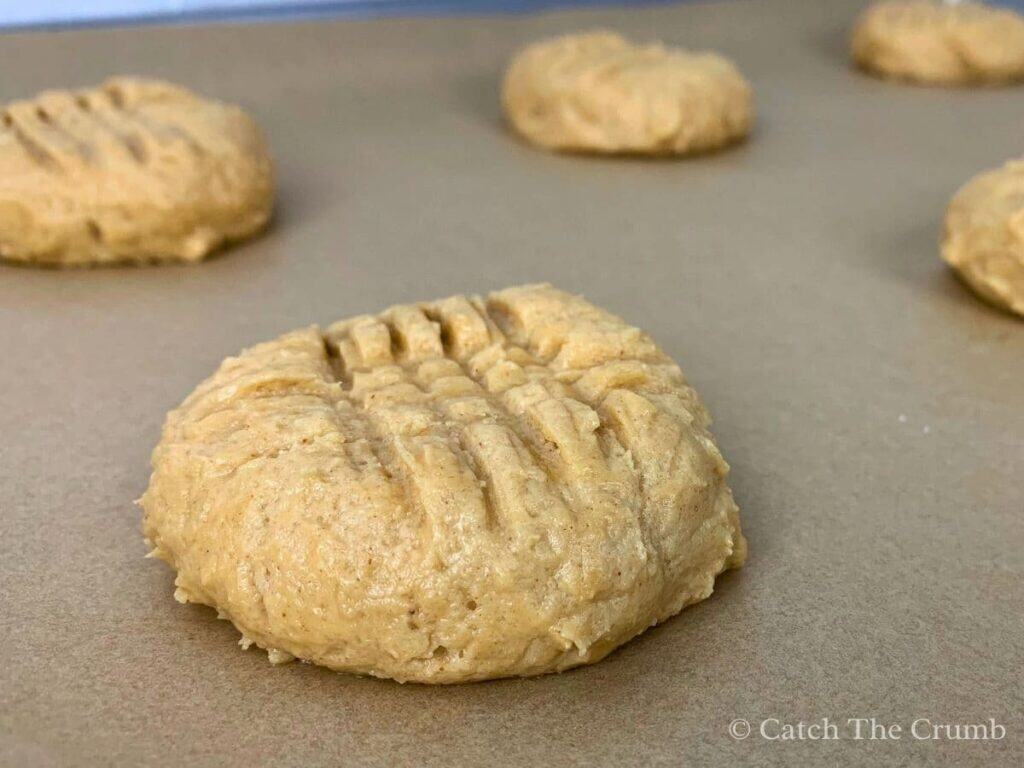 cookie dough balls on a baking sheet with a criss cross pattern