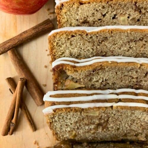 loaf of sourdough apple bread sliced on a cutting board next to an apple and cinnamon sticks