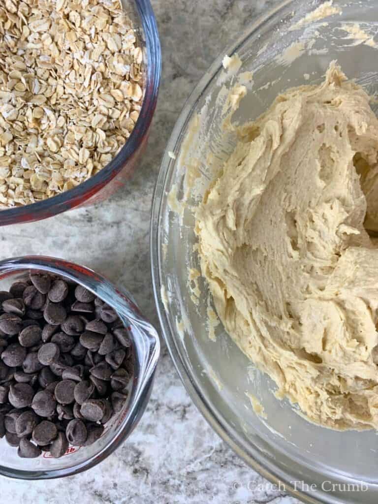 oatmeal and chocolate chips in mixing bowls next to a bowl containing the mixture