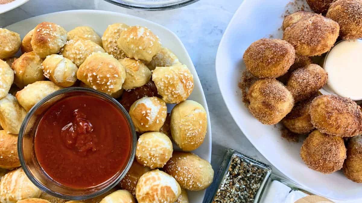 one plate of sourdough discard pretzel bites with pizza sauce and another covered in cinnamon sugar with a sweet glaze