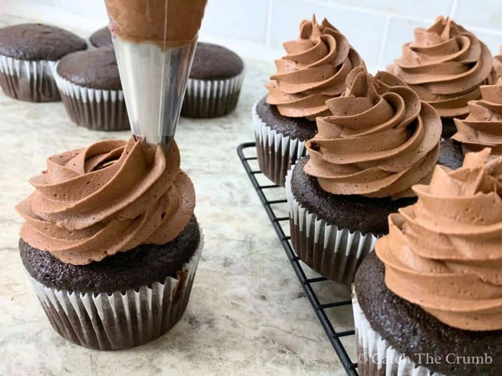 piping chocolate buttercream onto a sourdough chocolate cupcake