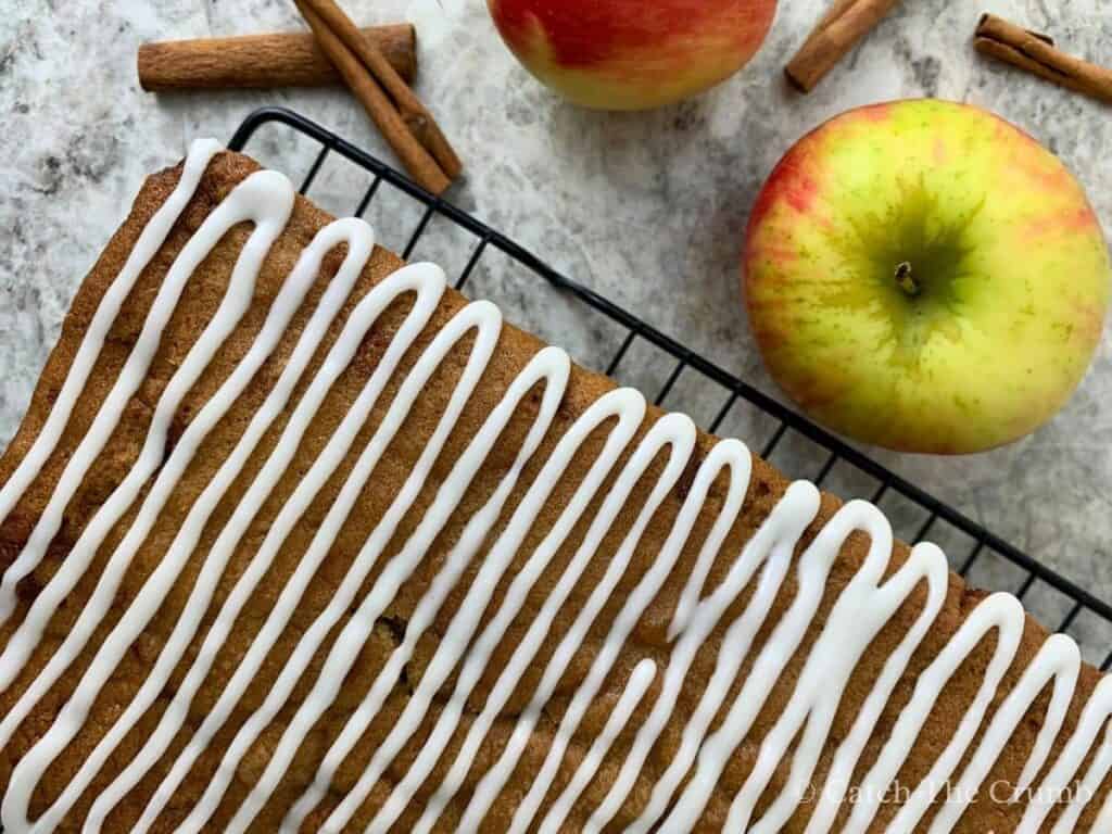 sourdough apple bread on a cooling rack next to apples and cinnamon sticks