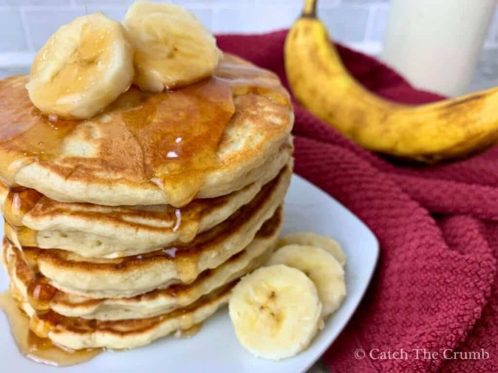stack of banana sourdough pancakes sitting on a plate covered in maple syrup