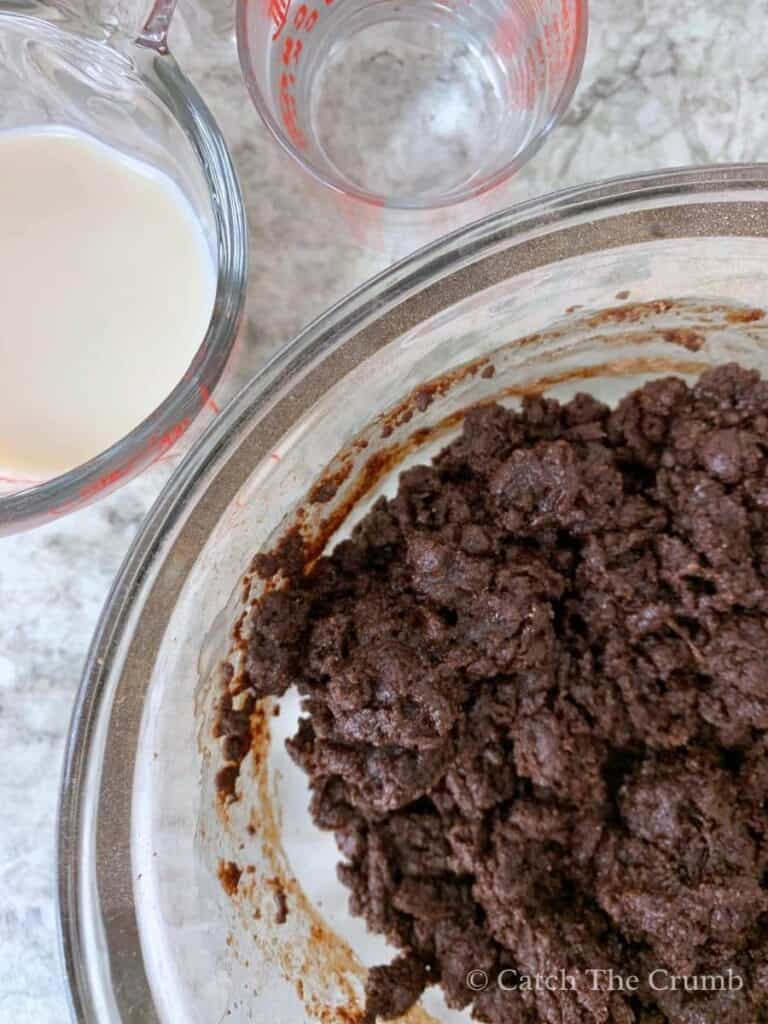 wet and dry ingredients mixed next to a mixing cup of milk and a mixing cup of water