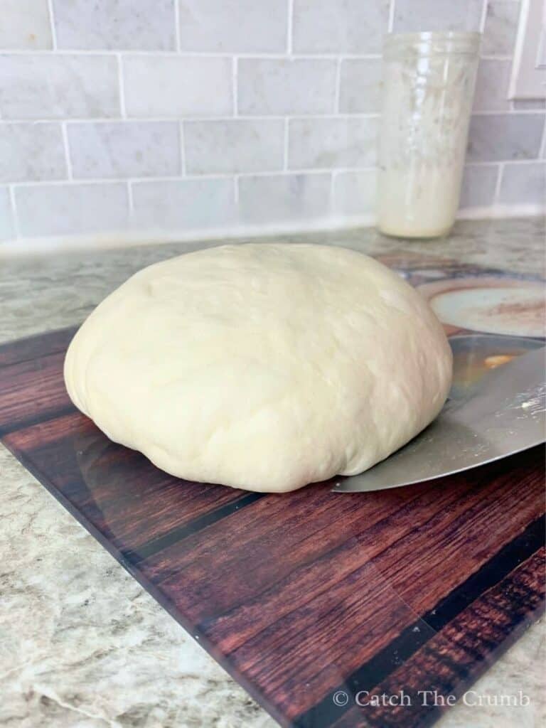 Gently pushing the dough up and away at a slight angle with a bench scraper