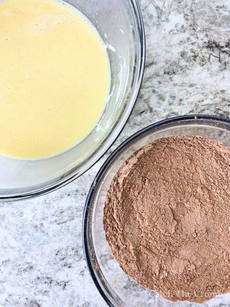 a mixing bowl with flour, cocoa powder, sugar, baking powder, baking soda, salt next to a bowl with eggs, oil, milk, vanilla extract, sourdough discard