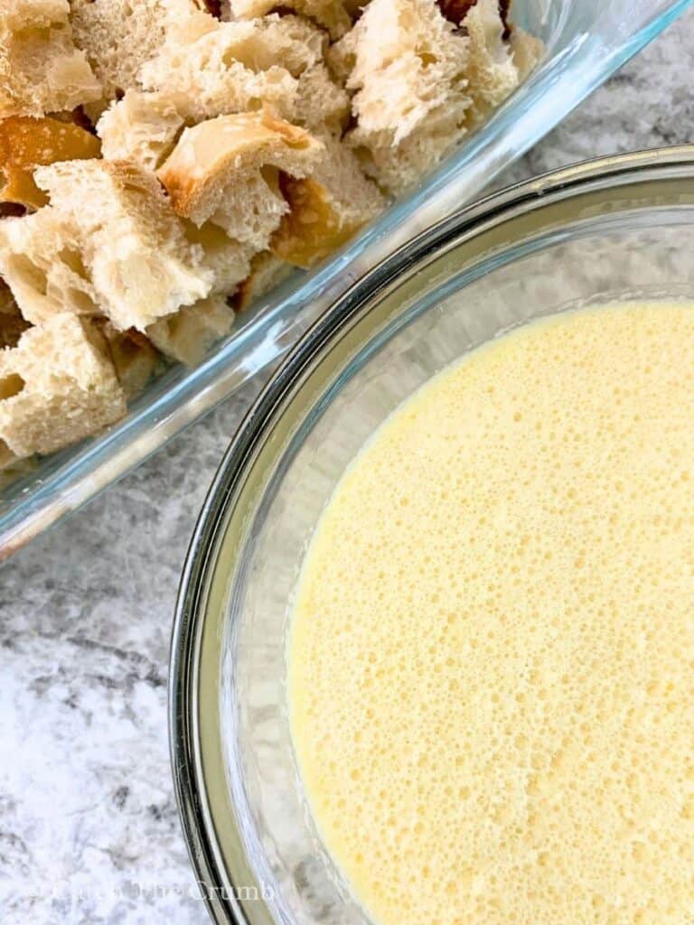 eggs, milk, melted butter, vanilla extract, and sugar in a mixing bowl next to sourdough chunks