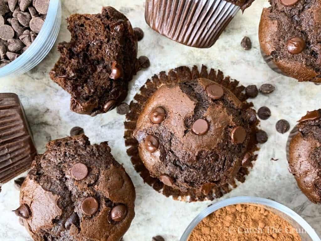sourdough chocolate muffins sitting on a countertop with chocolate chips scattered around