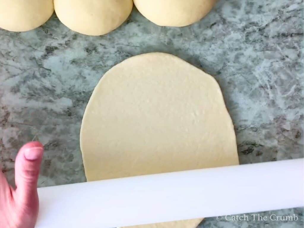 rolling the naan with a rolling pin into a circular shape